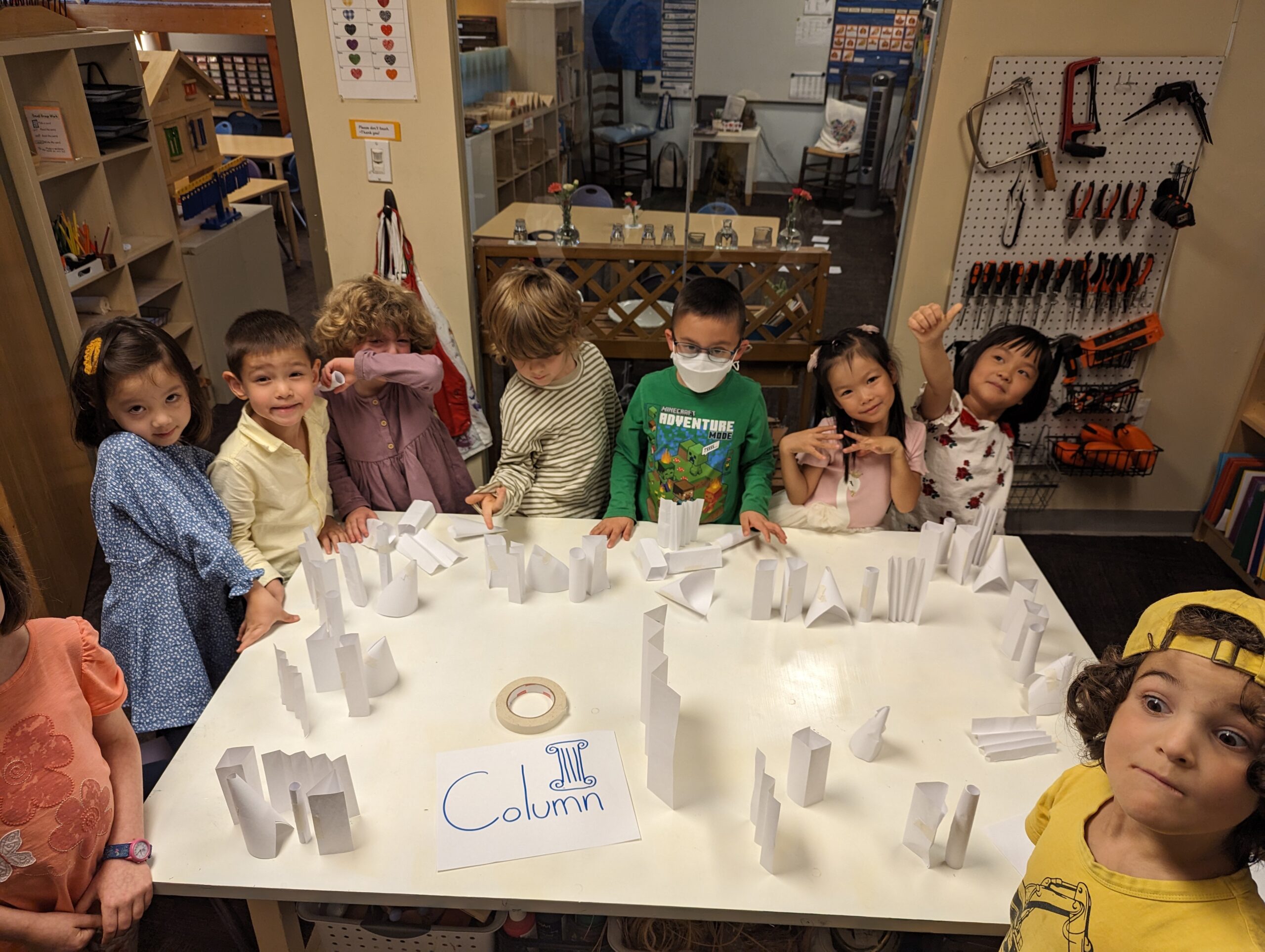 Students standing around a table full of paper columns of various shapes.